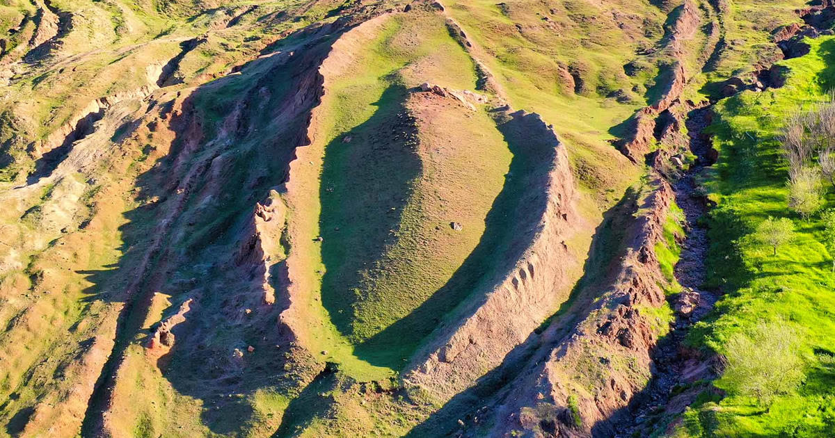 Aerial of the grass-covered boat-shaped Durupınar formation, rimmed by eroded red earth.