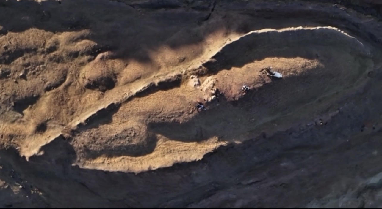 Overhead view of the boat-shaped Durupınar mound with small figures and field gear on the ground.